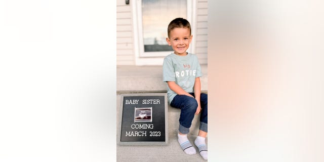 Cameron Clark, 4, is pictured smiling with a sign announcing his baby sister's then-imminent arrival. 