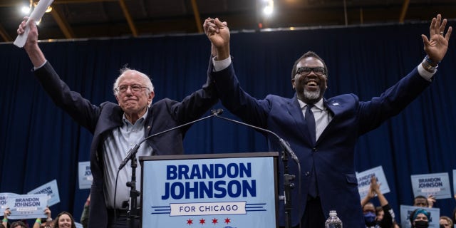 Progressive mayoral candidate Brandon Johnson and Bernie Sanders raise their hands to a crowd of supporters at Johnson's rally at the UIC Forum on March 30, 2023.