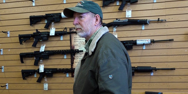 Gun store manager Bruce Smith, wall of rifles behind him