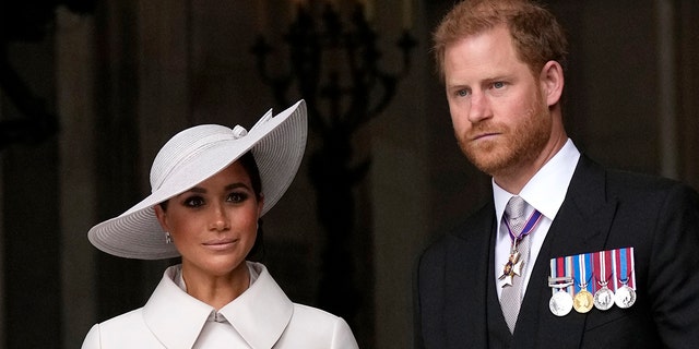 Meghan Markle in a white coat dress and a matching white hat with Prince Harry in a suit and tie