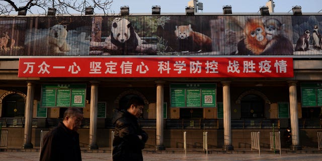 Men walk past a banner hung at the Beijing Zoo on Feb. 10, 2020. The banner reads "Stay focused and united, have faith and confidence, with scientific prevention and control, we can beat the epidemic." China has decided not to participated in a UN wildlife survey aimed at preventing future pandemics due to zoonotic transmission.