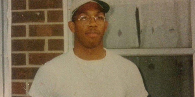 Damion Cooper wearing a white T-shirt and ball cap, standing in front of a brick home
