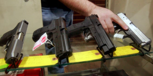 man holding gun that's in display case with other guns