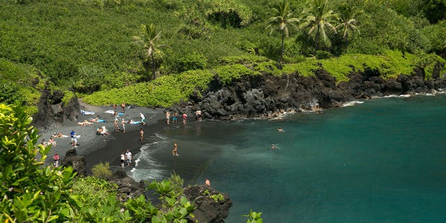 People spend time on the black sand beach at Waianapanapa State Park in Hana, Hawaii, on Sept. 24, 2014. Taking care of Hawaii's environment costs money and now the state wants tourists to help pay for it.