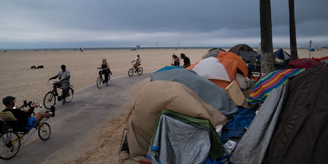 People ride their bikes past a homeless encampment in a neighborhood of Los Angeles on June 29, 2021. Democratic Mayor Karen Bass announced that she would recommend spending what she called a record $1.3 billion next year to tackle the city’s homeless crisis.