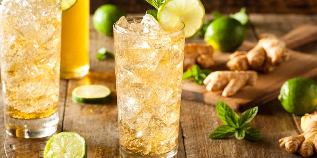 Glass of ginger ale next to ginger root, limes and mint.