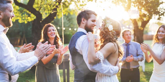 Wedding reception outside in the backyard. Bride and groom with a family dancing.