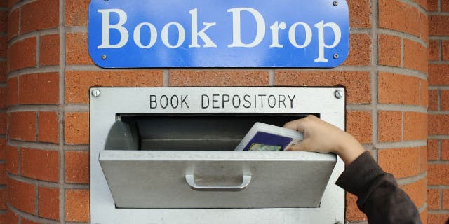 A hand returns a borrowed item at library book drop box.