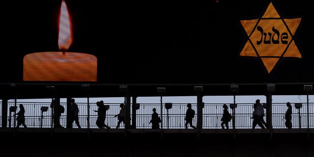 Ljudi hodaju duž mosta ispod reklamnog panoa koji prikazuje žutu Davidovu zvijezdu na kojoj piše Židov na njemačkom tijekom godišnjeg Dana sjećanja na holokaust u Ramat Ganu, Izrael, 18. travnja 2023. Izraelski Dan sjećanja obilježava šest milijuna ubijenih židovskih žrtava od strane nacističke Njemačke.
