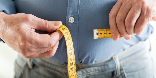 A man measures his waist with a tape measure.