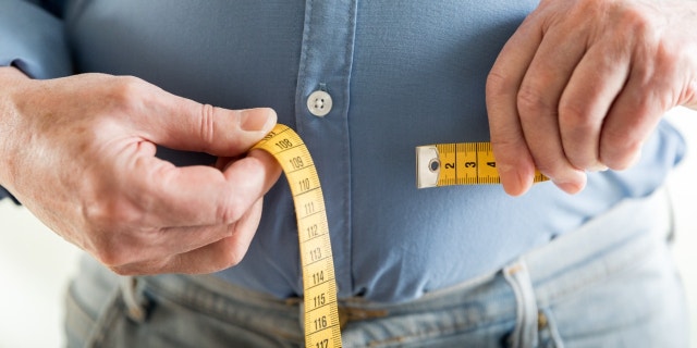 A man measures his waist with a tape measure.