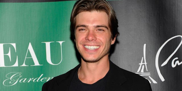 Matthew Lawrence wears black outfit in front of a green background