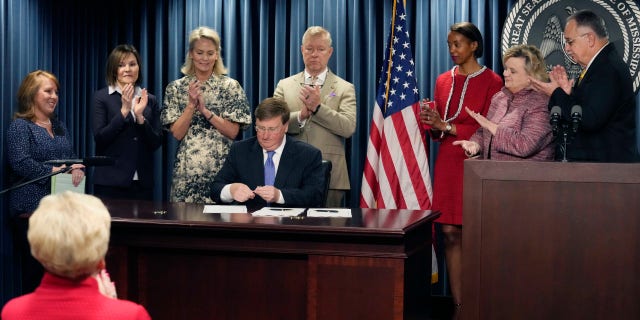 Mississippi Gov. Tate Reeves is surrounded by applauding lawmakers