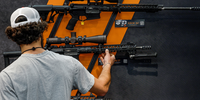 a man looks at rifles on the wall at a National Rifle Association event