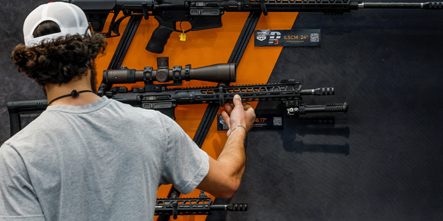 a man looks at rifles on the wall at a National Rifle Association event