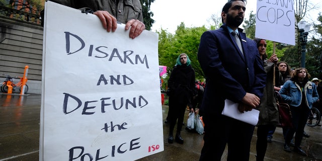 Protesters hold signs reading "disarm cops" and "defund the police" in Portland, Oregon