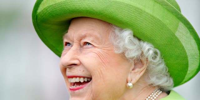 Königin Elizabeth lächelt breit, während sie einen leuchtend grünen Mantel mit passendem Hut trägt.