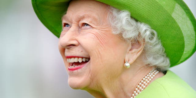 Queen Elizabeth gives a big smile while wearing a bright green coat with a matching hat.