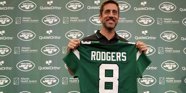 Aaron Rodgers holds up the Jets jersey at a conference