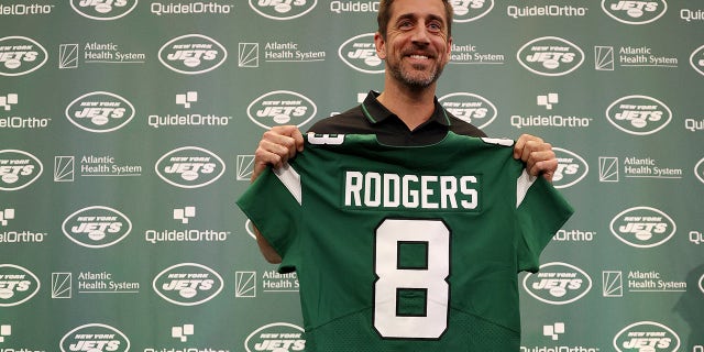 Aaron Rodgers holds up the Jets jersey at a conference