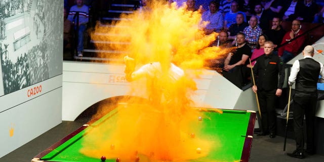 A 'Just Stop Oil' protester jumps on the table and throws orange powder during a World Snooker Championship match in Britain on April 17, 2023. 