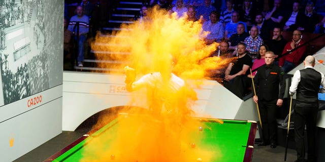 A 'Just Stop Oil' protester jumps on the table and throws orange powder during a World Snooker Championship match in Britain on April 17, 2023. 
