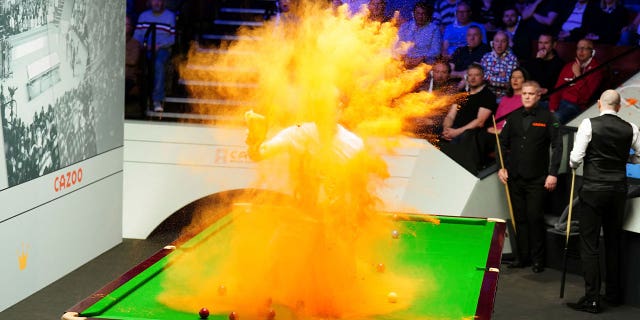 A 'Just Stop Oil' protester jumps on the table and throws orange powder during a World Snooker Championship match in Britain on April 17, 2023.