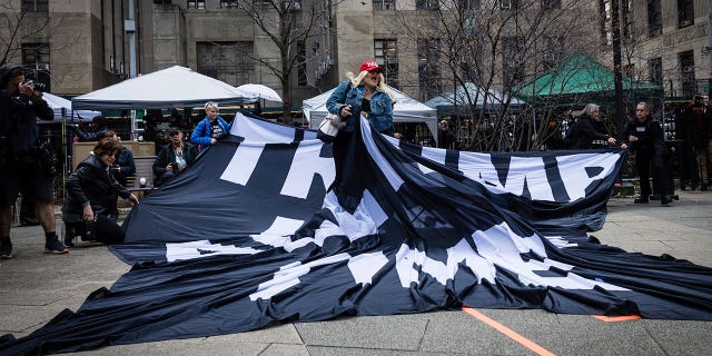 A supporter of former President Donald Trump pulls up an anti-Trump banner off the ground near protests in front of the Manhattan courthouse.