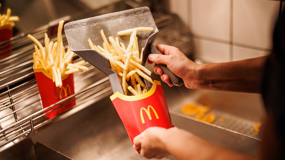 McDonald's kitchen employee shovels fries in a medium red container.