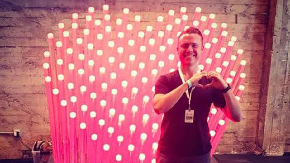 Bob Lee makes heart shape with his hands in front of a light display shaped like a heart