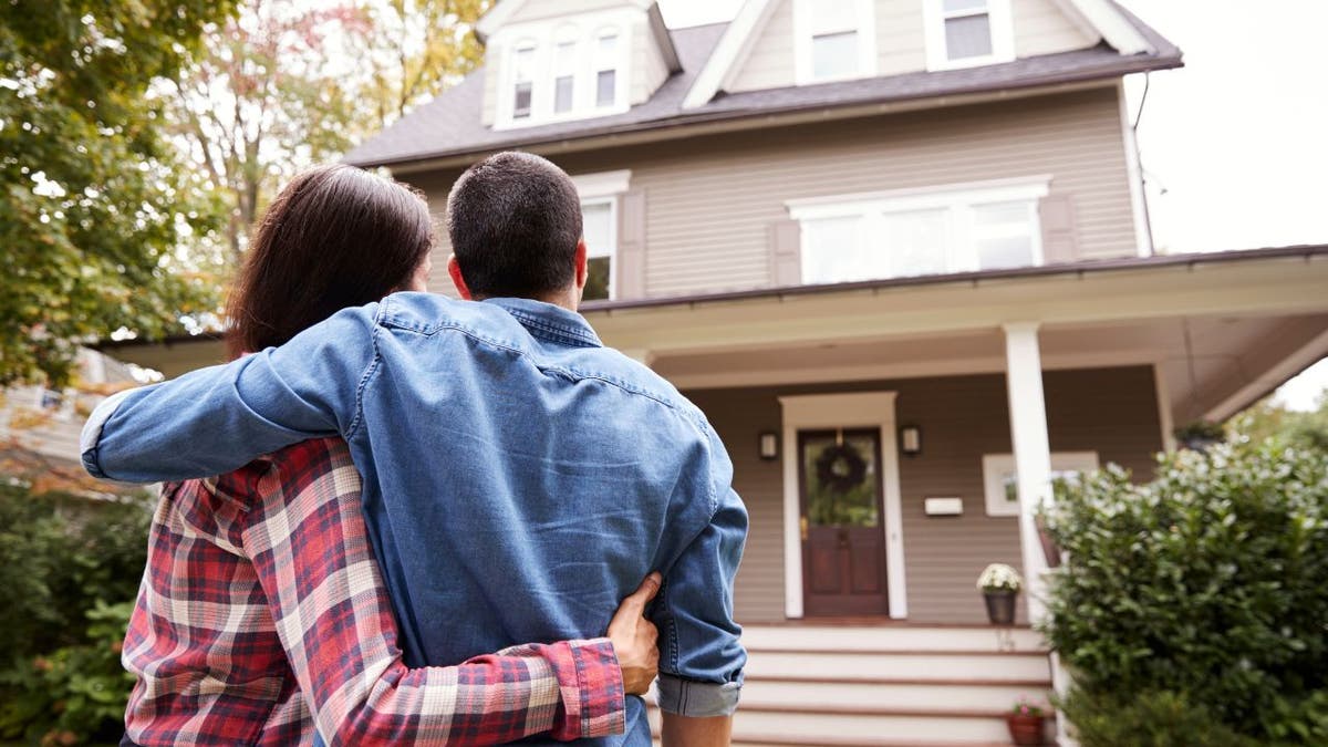 Couple hugs as they look at the front of a house 