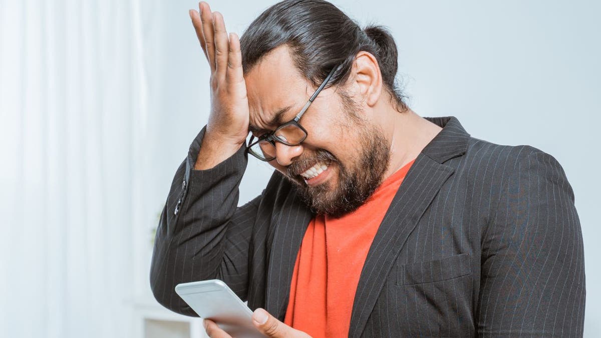 Stressed man face palms while on his phone 