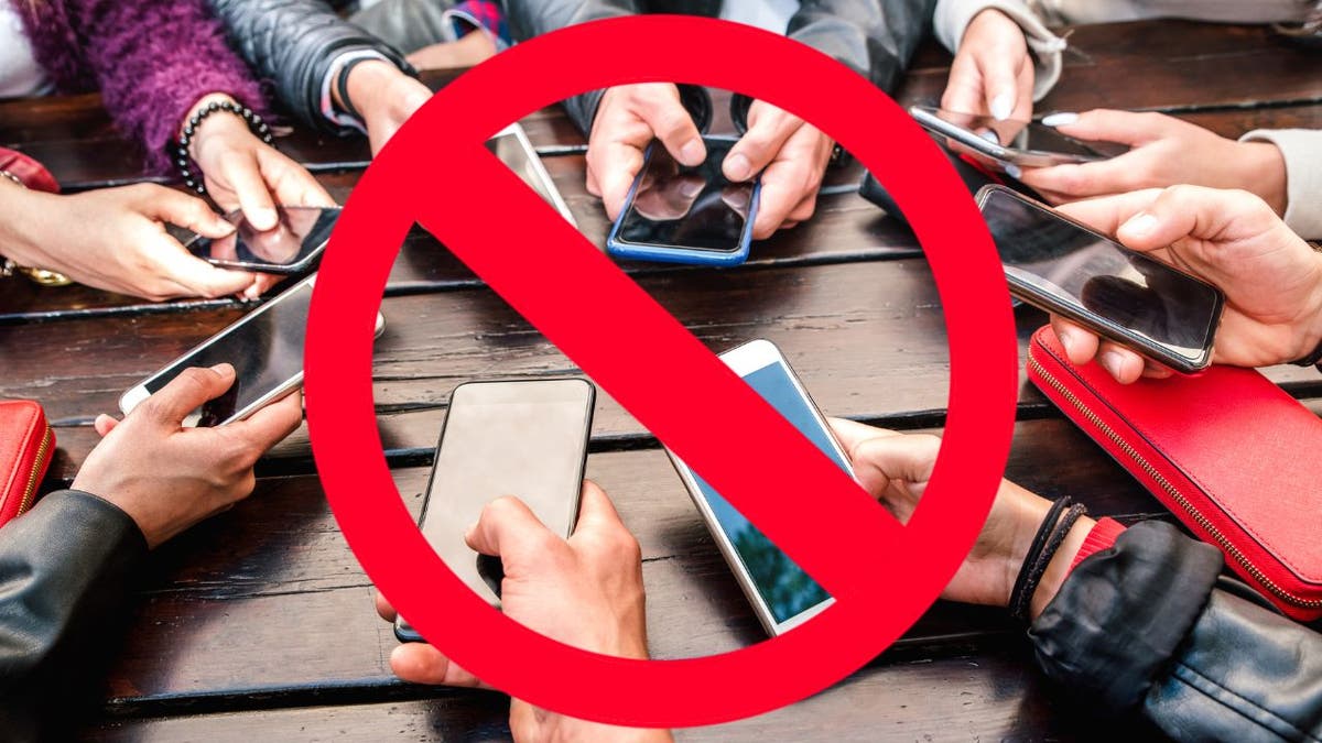A group of people holding their smartphones together with a general prohibition sign over them.
