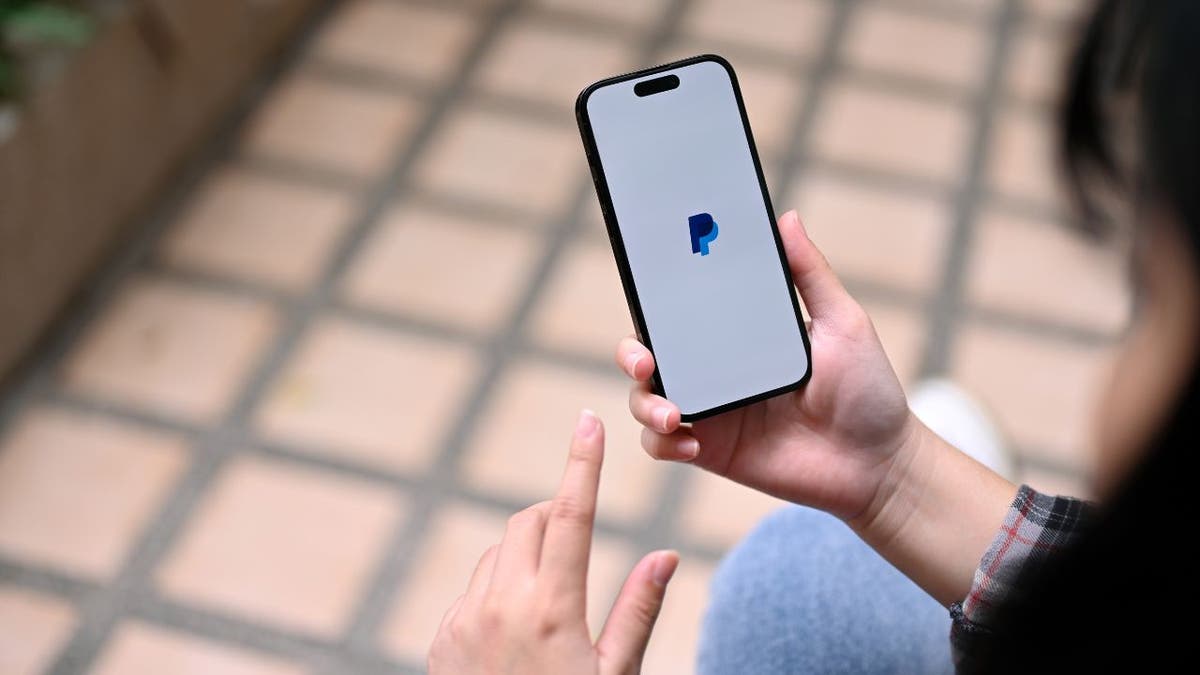 Woman holding her phone while loading the PayPal app.