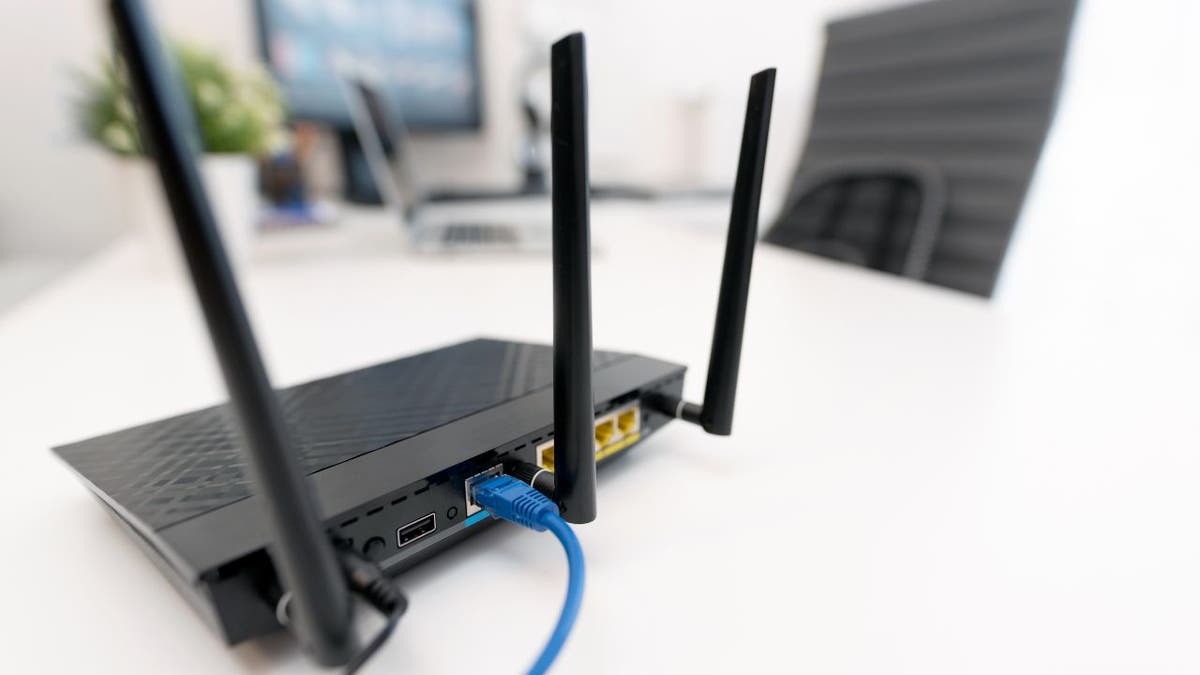 Black wifi router on white desk near computer monitors 