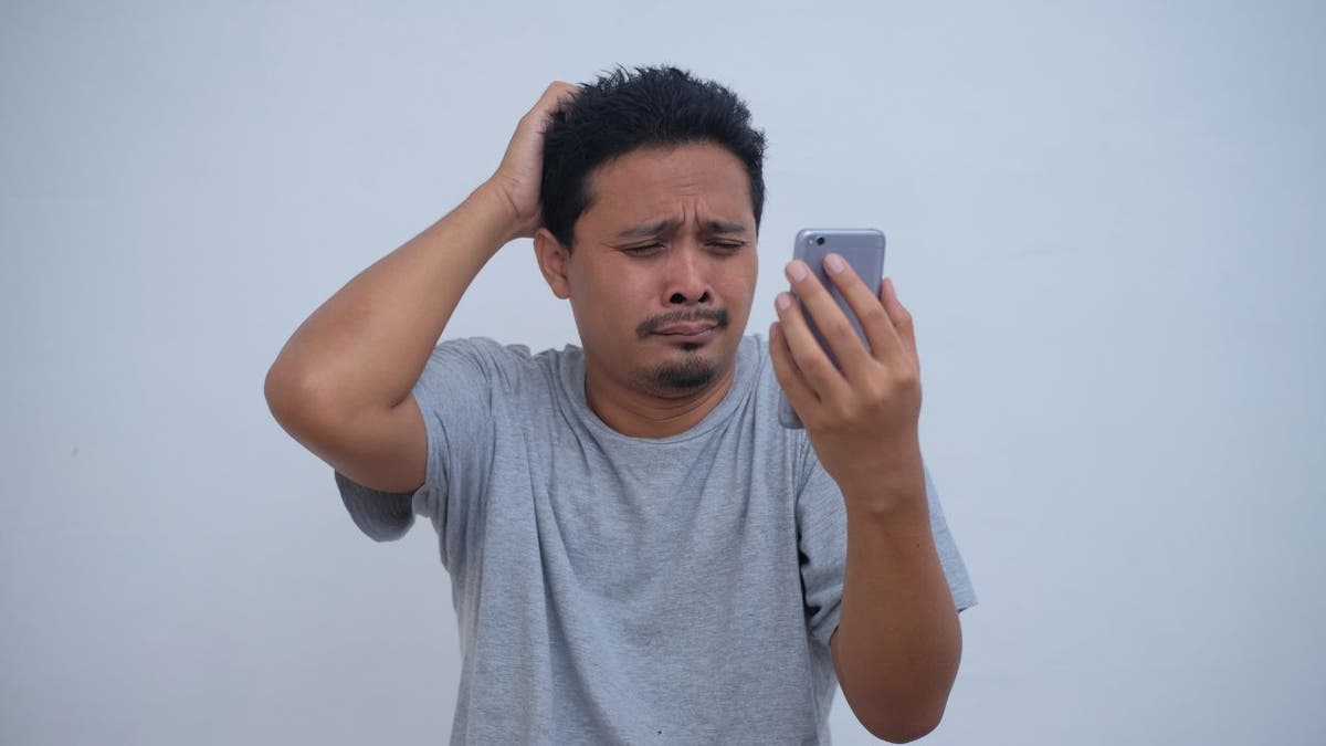 Upset man rubs his head while on his phone