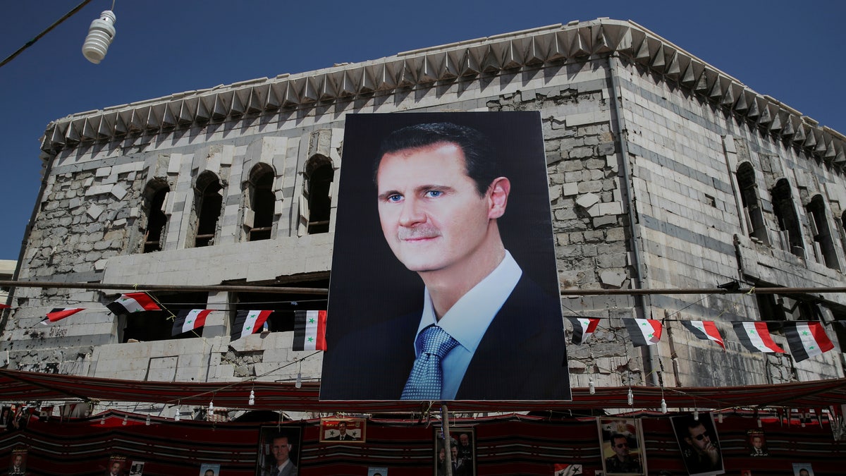 FILE PHOTO: A man walks past a banner depicting Syrian president Bashar al-Assad in Douma, outside Damascus, Syria, September 17, 2018. 