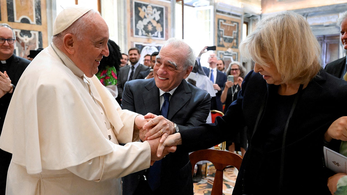 Pope Francis in his white robe holds the hands of Martin Scorsese's wife Helen as Martin looks on and adds his hand to the pile
