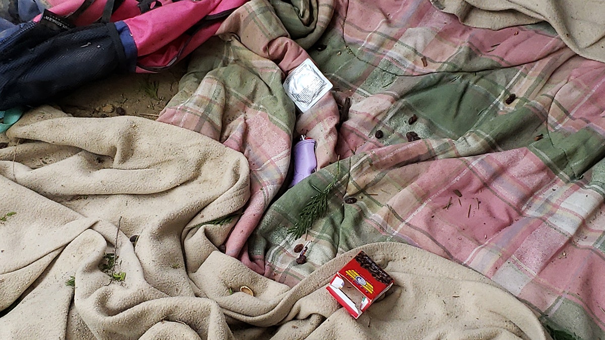 Unused condom packet next to purple lighter on pink and green flannel blanket