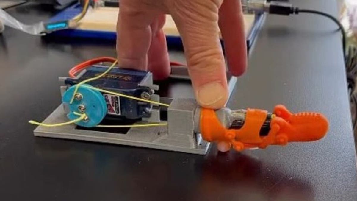 Orange 3D-printed prosthetic pinky on a contraption with man's hand on top