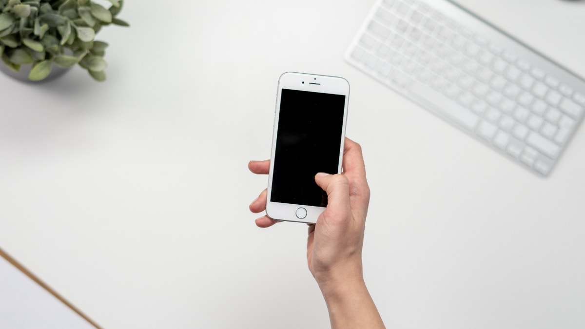 A person holing their phone over a white desk.