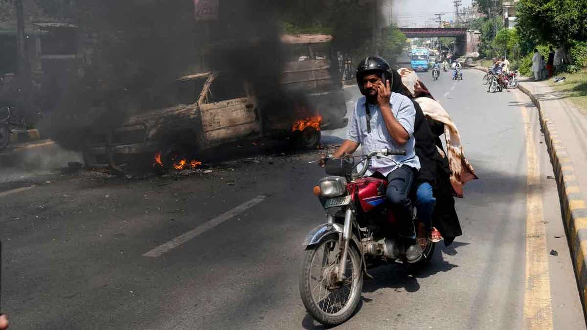 A motorcyclist drives past a burning vehicle