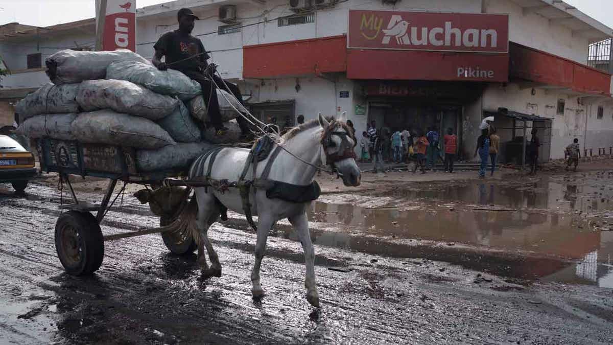 A man drives his horse-drawn cart past a supermarket