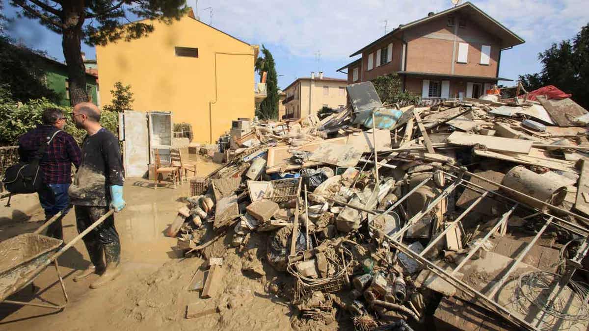 Volunteers clear mud as household goods are piled on the side of a street in Faenza, Italy, 