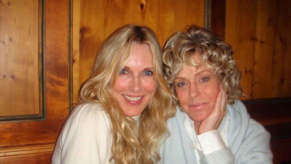 Farrah Fawcett wearing a sea green swear and a white shirt leaning next to Alana Stewart in a white sweater