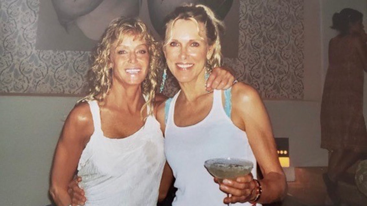 Farrah Fawcett and Alana Stewart wearing white tank tops while Alana holds a martini glass