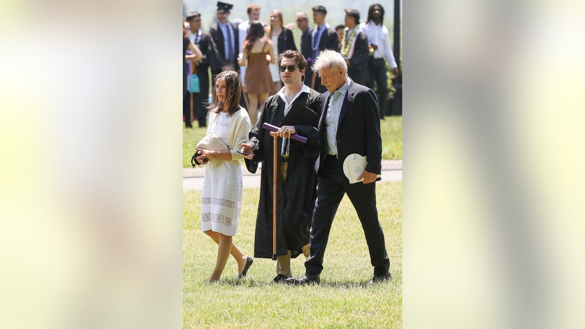 Calista Flockhart and Harrison Ford walk with son, Liam, holding a cane, at his college graduation.