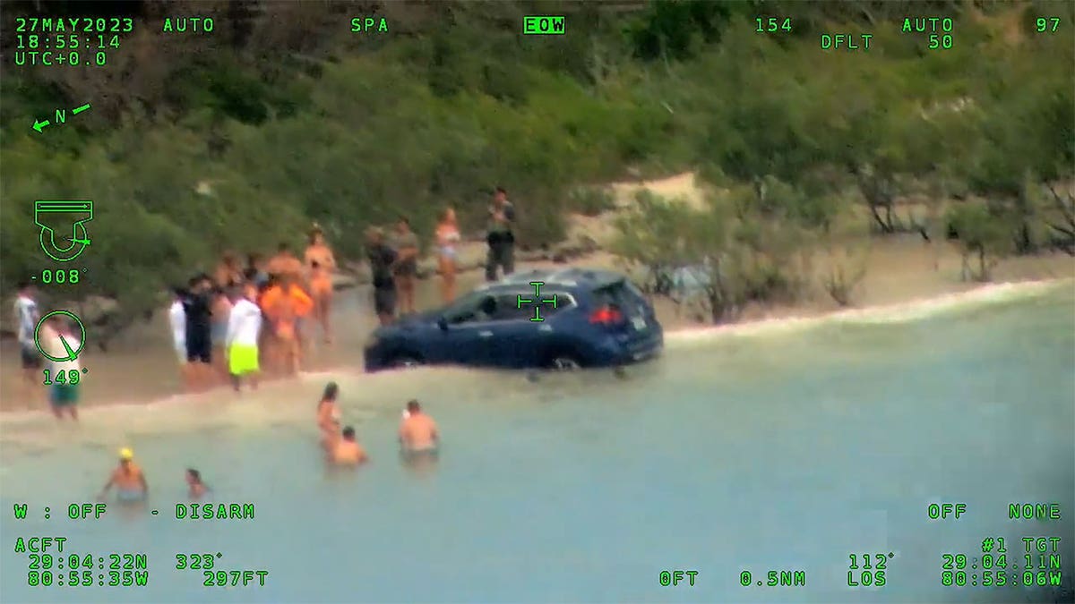 SUV in the water while a crowd stands around.