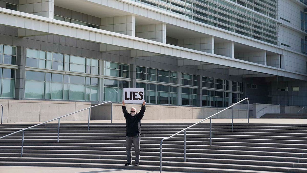 Bill Christeson holds up a sign on the steps of the federal courthouse in Central Islip