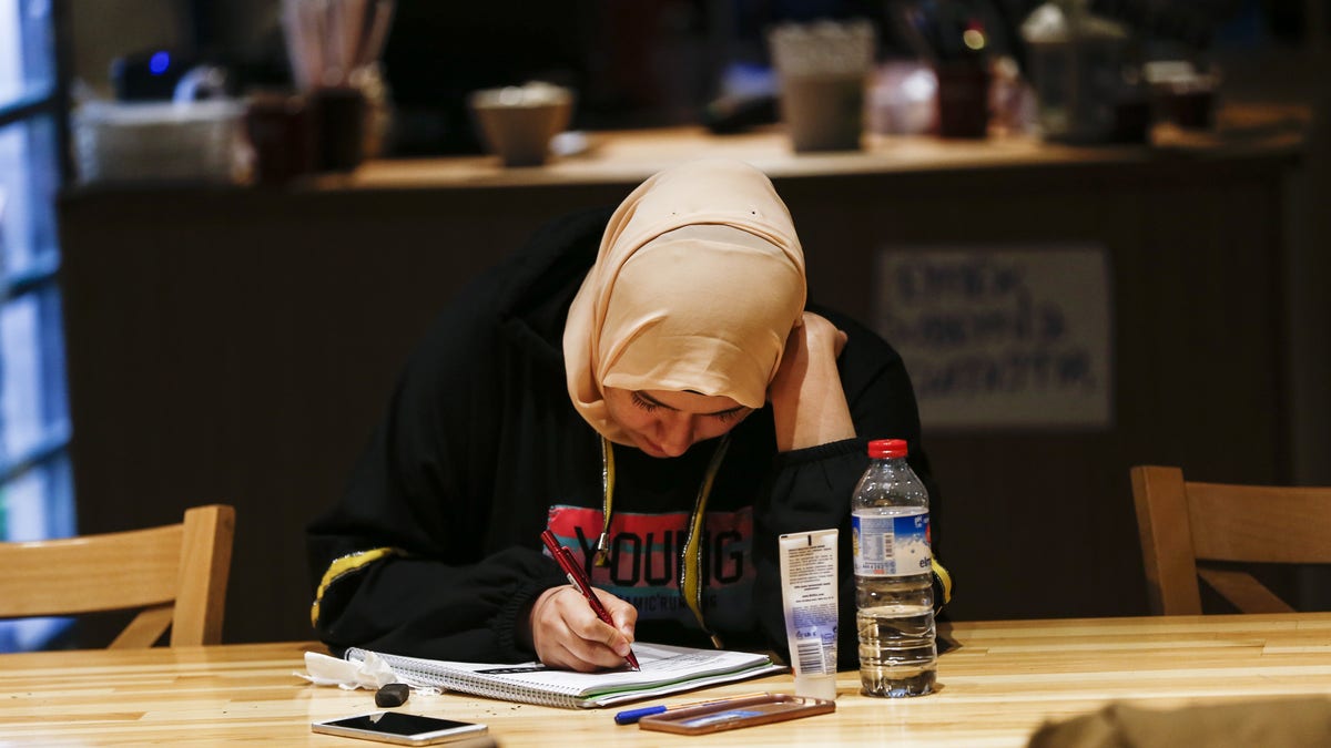 A student writes in a notebook at a table in a library-like cafeteria in Ankara, Turkey.